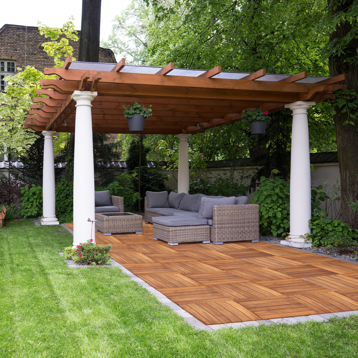 Dalles de terrasse en bois d'acacia, couleur miel, disposées en motif chevron, sous une pergola avec mobilier de jardin moderne