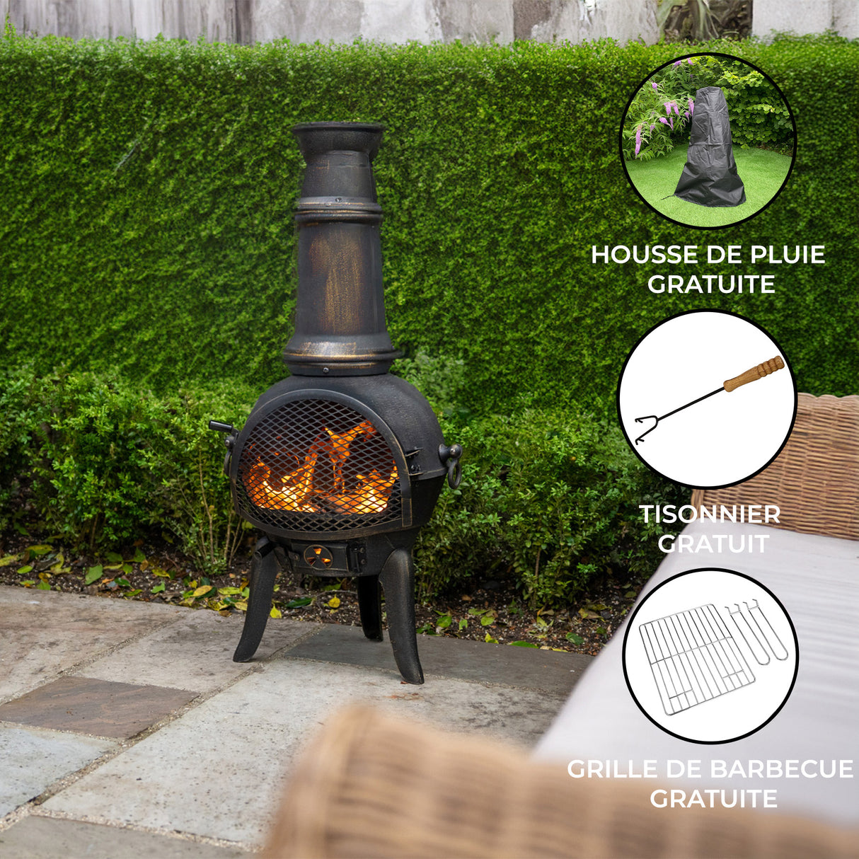 Cheminée de jardin en fonte noire avec cheminée, flammes vives, sur un patio en pierre, entourée de verdure et de mobilier en osier