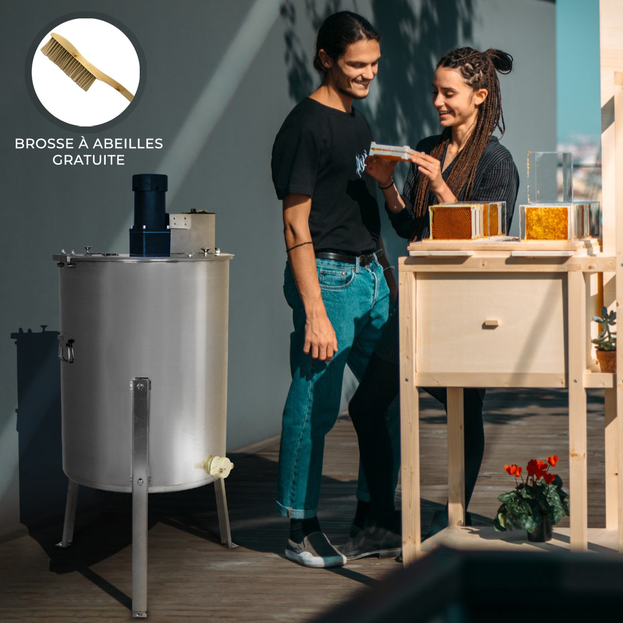 Extracteur de miel électrique en acier inoxydable, avec un coupleur bleu, utilisé par un couple souriant dans un environnement lumineux