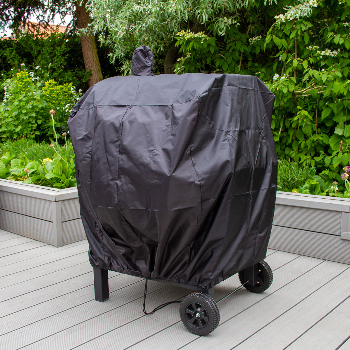 Housse de barbecue XL noire en tissu résistant, ajustée sur un grill sur roues, protégée par une verdure luxuriante en arrière-plan