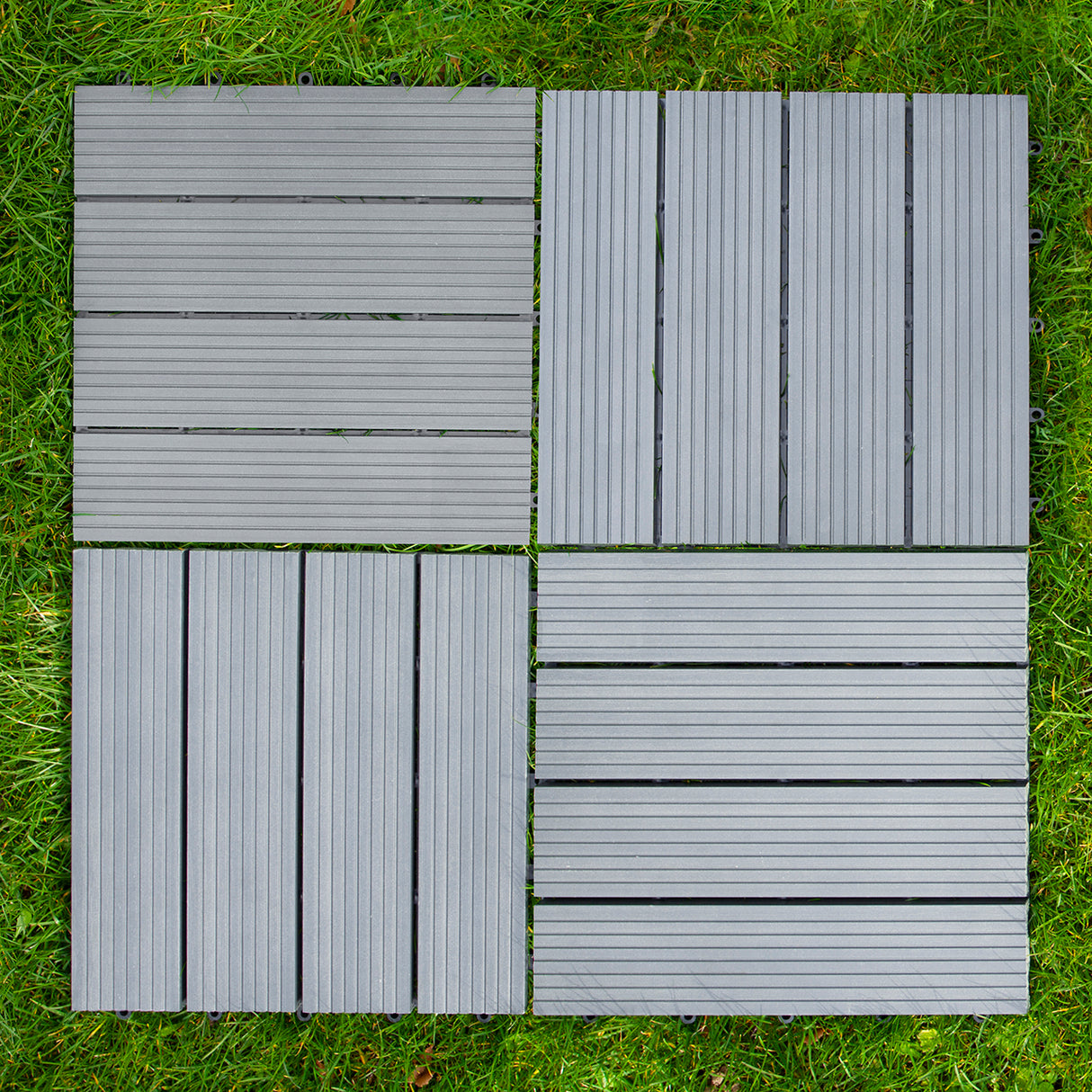 Dalles en bois composite gris de 30 x 30 cm, avec texture striée, disposées sur une surface herbeuse, offrant un aspect moderne et durable