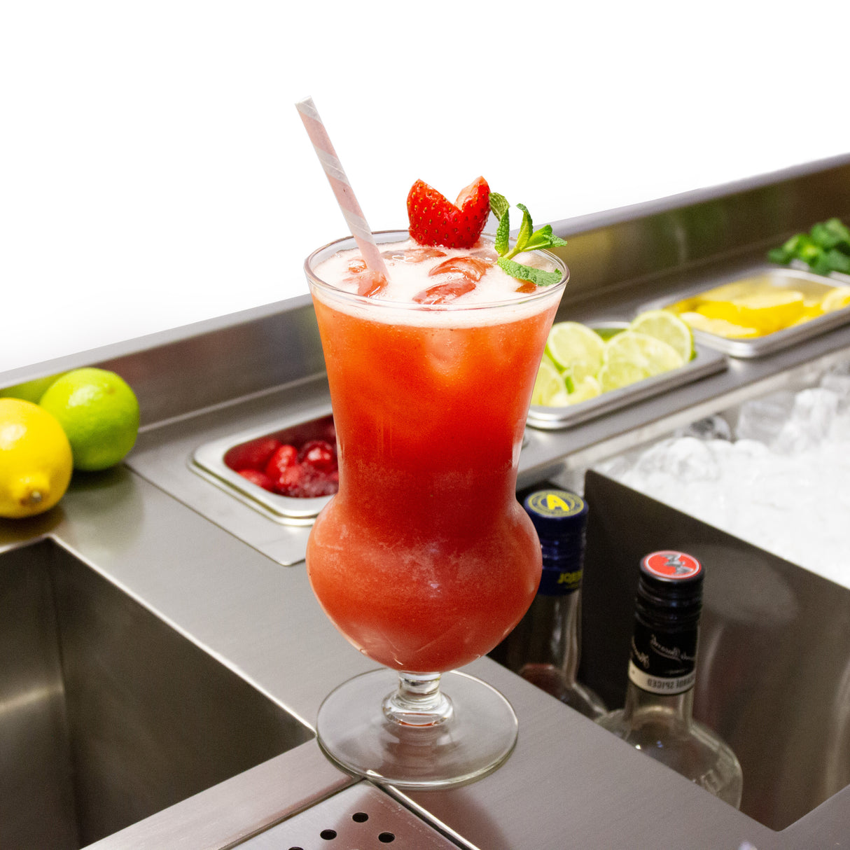 Cocktail coloré dans un verre élégant, garni de fraises et de menthe, avec des fruits frais en arrière-plan sur un bar en acier inoxydable