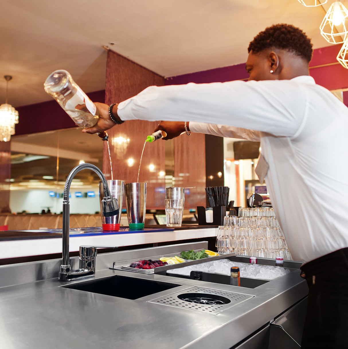 Barman versant des ingrédients colorés dans un shaker en acier inoxydable sur une station de bar à cocktails moderne et élégante