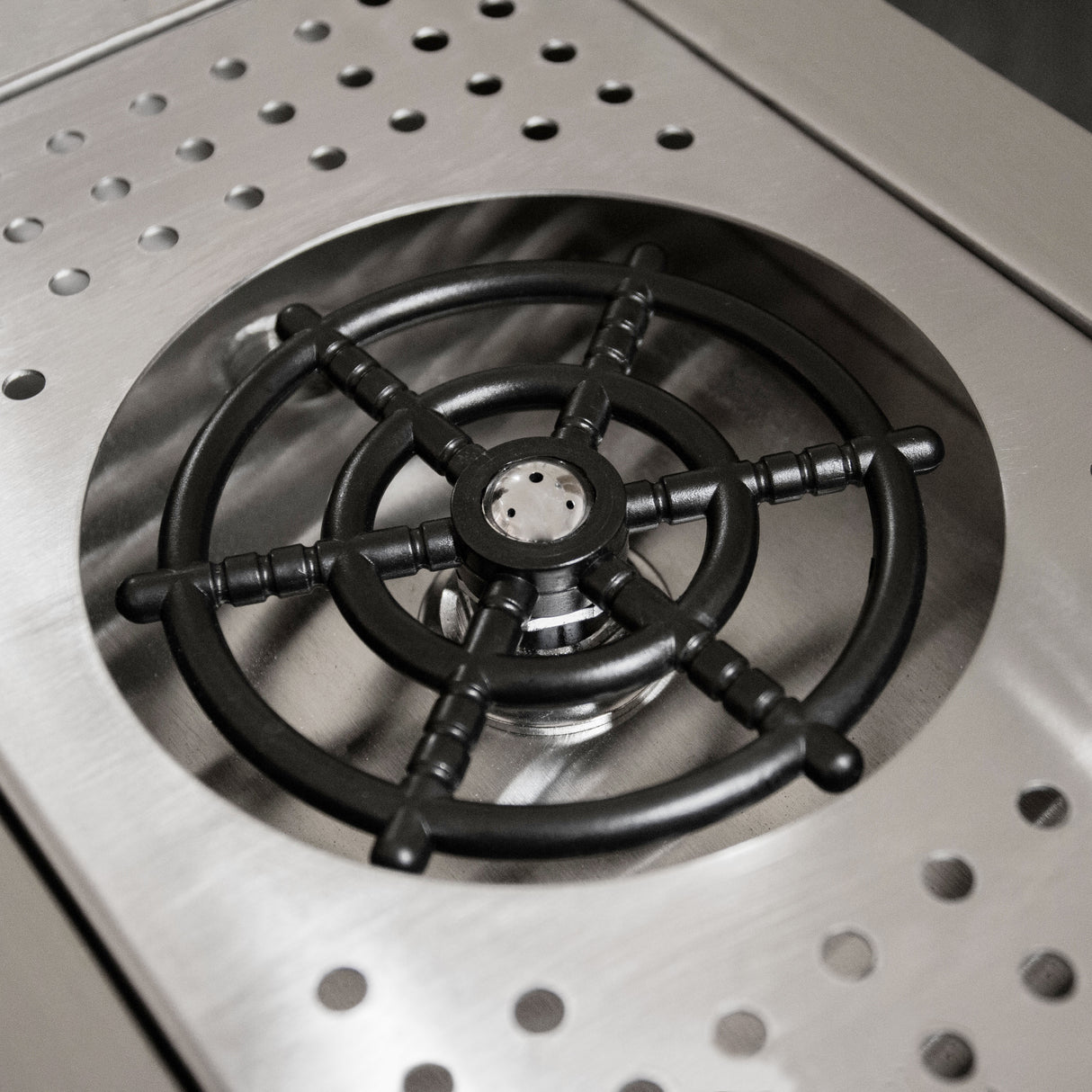 Plancha en acier inoxydable avec un brûleur noir en fonte, surface lisse et perforée pour une cuisson efficace et élégante