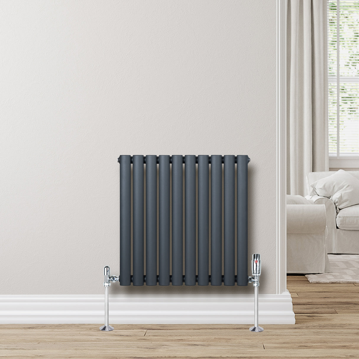 Radiateur à colonnes ovales gris anthracite, 600 x 600 mm, installé contre un mur clair, avec des pieds en métal chromé