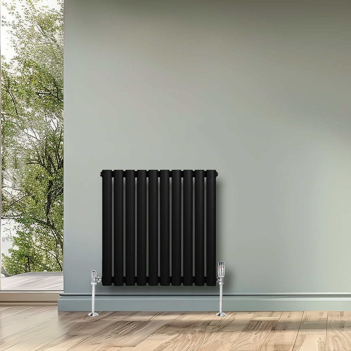 Radiateur à colonnes ovales noir, 600 x 600 mm, installé sur un mur gris, avec un sol en bois clair et une vue sur la nature à l'extérieur