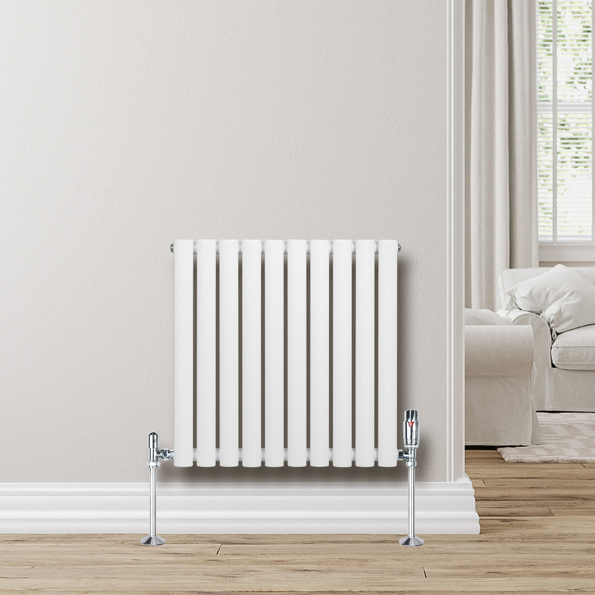 Radiateur à colonnes ovales blanc, 600 x 600 mm, avec des pieds chromés, installé contre un mur clair dans un intérieur moderne