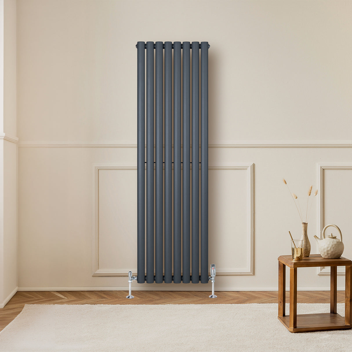 Radiateur à colonnes ovales gris anthracite, élégant et moderne, installé sur un mur beige, avec un meuble en bois à proximité