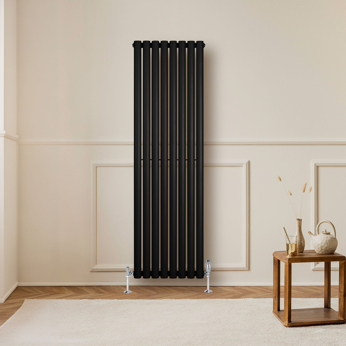 Radiateur à colonnes ovales noir, 1600 x 480 mm, installé sur un mur beige, avec un sol en bois et une table en bois à proximité