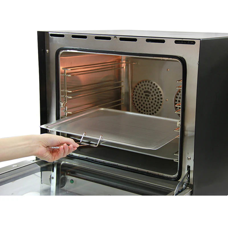 Four à convection KuKoo de 60 cm avec double ventilateur, intérieur en acier inoxydable, grille en métal et plateau en aluminium, main tenant le plateau
