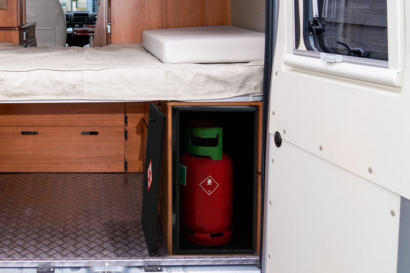 Réservoir de gaz rouge avec étiquette de sécurité, placé dans un compartiment noir sous un lit en bois dans un véhicule aménagé