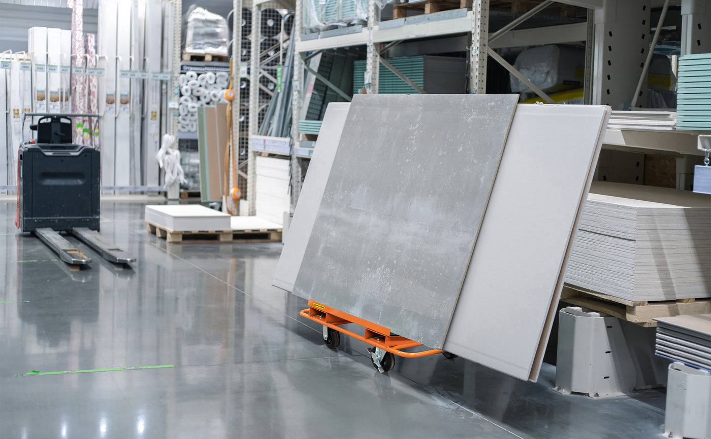 Panneaux de béton gris clair sur un chariot orange dans un entrepôt, avec des étagères remplies de matériaux en arrière-plan