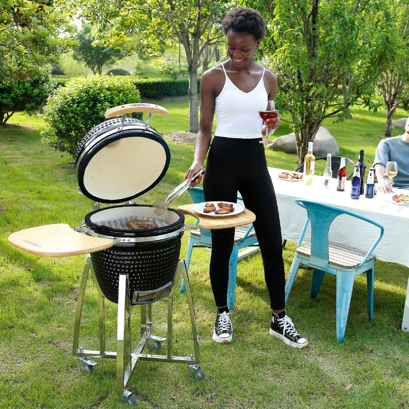 Barbecue au charbon de bois Kamado de 53,3 cm, avec couvercle ouvert, grillant des viandes, entouré d'un jardin verdoyant