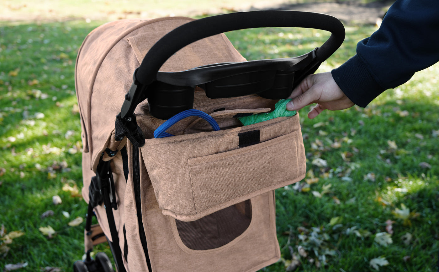 Poussette beige avec un rangement pratique, une main tenant un parapluie vert, sur un fond de pelouse verte parsemée de feuilles