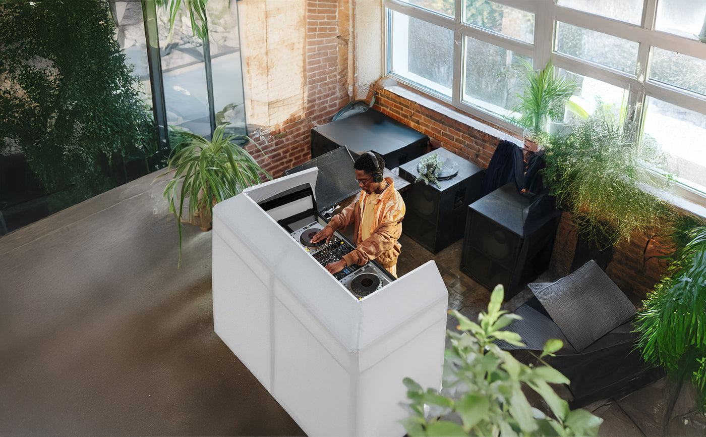 DJ en action dans un espace moderne avec des plantes, mixant sur une table de mixage blanche, lumière naturelle abondante