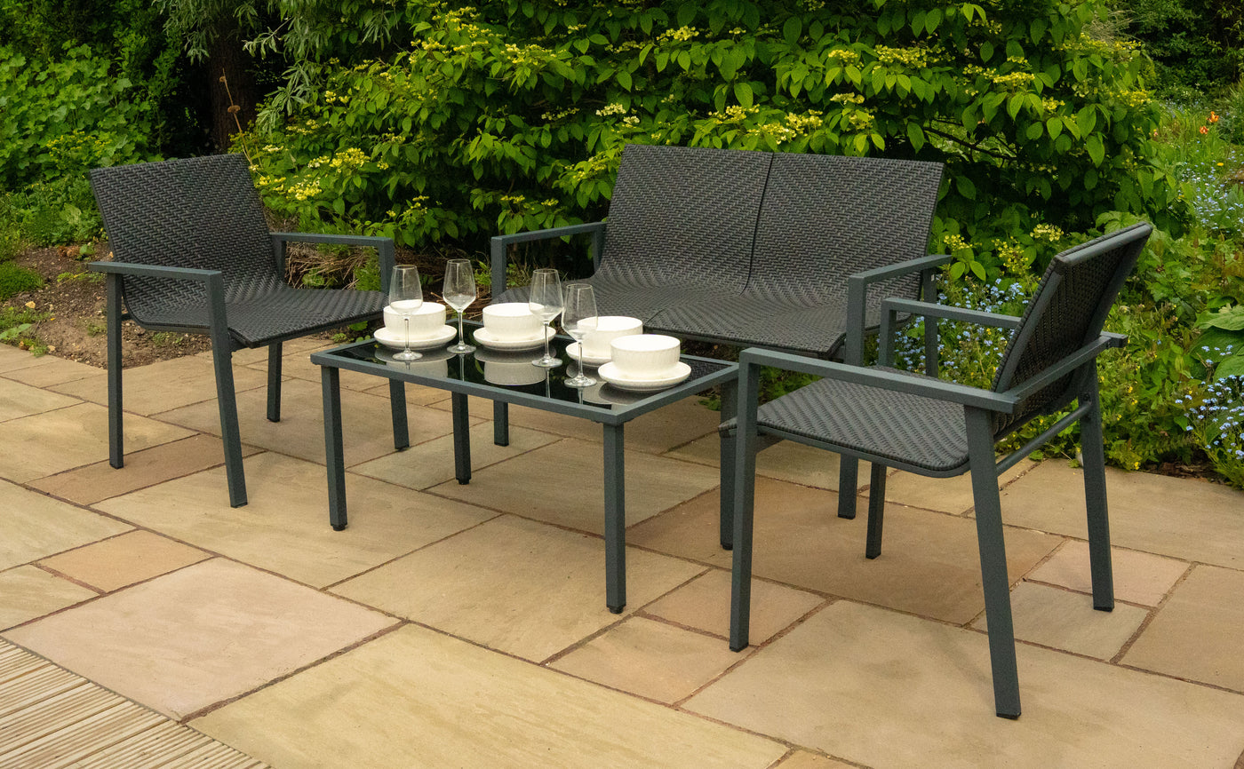 Ensemble de mobilier de jardin en résine tressée grise, comprenant deux chaises et une table en verre, décoré de vaisselle blanche