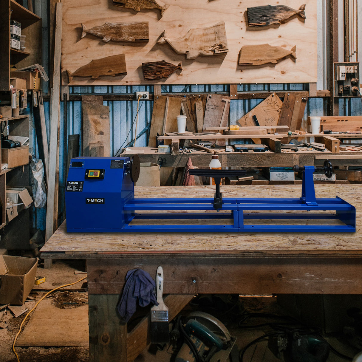 Tour à bois T-Mech de couleur bleue, positionnée sur un établi en bois, entourée d'outils et de matériaux de travail en atelier