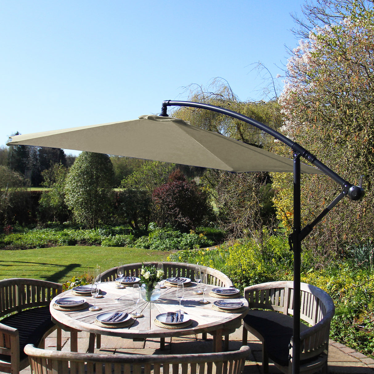 Parasol déporté beige de 3 m, avec structure noire, offrant une ombre élégante sur une table en bois entourée de verdure