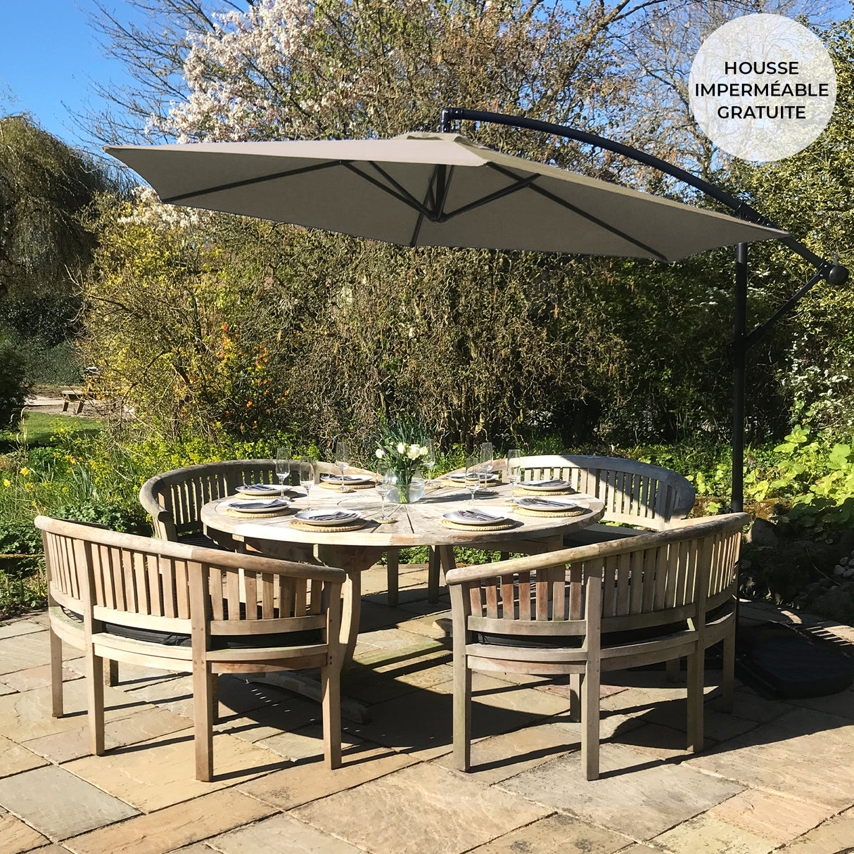 Parasol déporté beige de 3 m, installé au-dessus d'une table en bois entourée de chaises, dans un jardin verdoyant ensoleillé