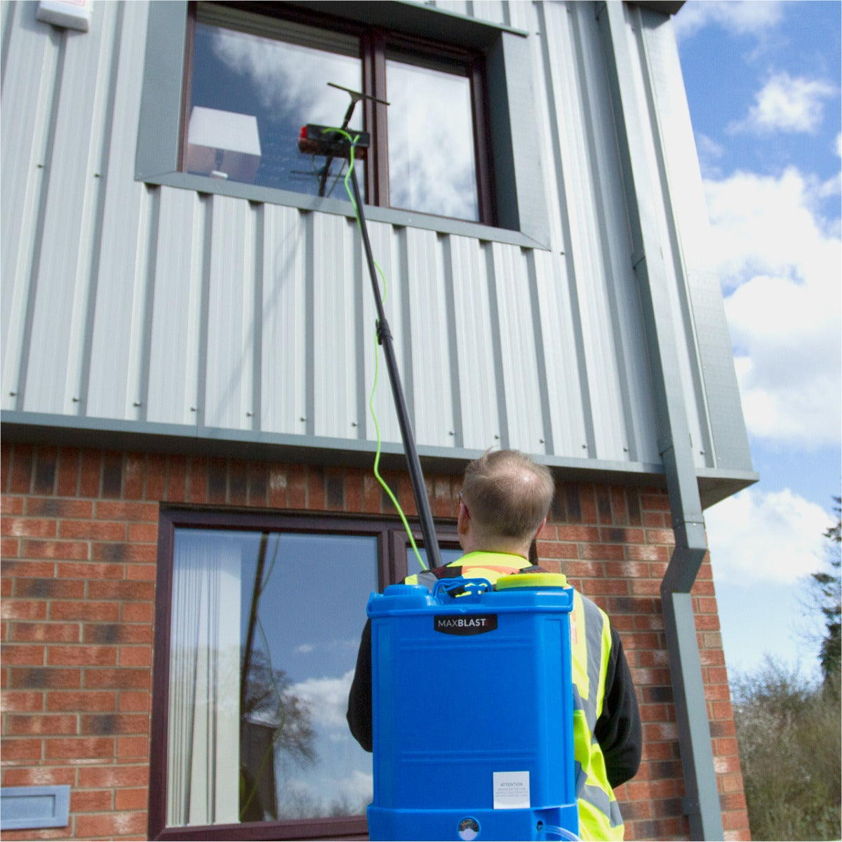Réservoir d'eau bleu de 16 L porté en sac à dos, avec une perche de nettoyage verte de 6 m, nettoyant une fenêtre d'immeuble moderne