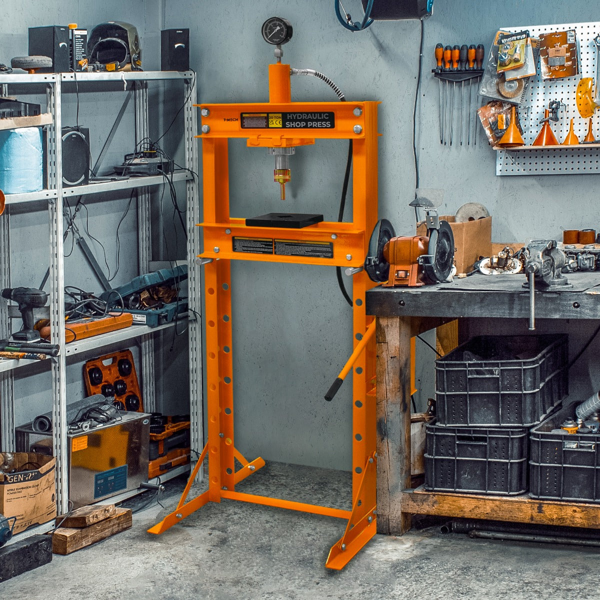 Presse hydraulique d'atelier orange sur pieds, robuste, avec un cadre en métal et un vérin, entourée d'outils dans un atelier bien rangé