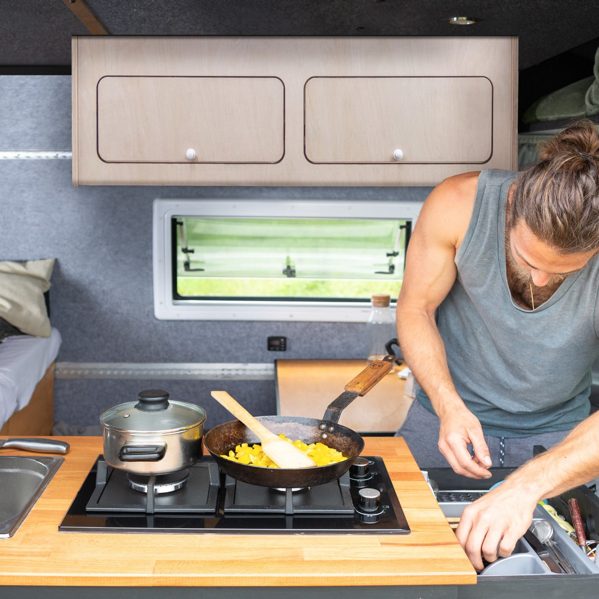 Armoire de rangement en bois clair, intégrée dans un camping-car, avec un plan de travail en bois et des ustensiles de cuisine en action