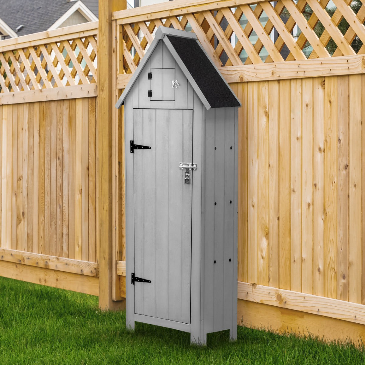 Abri de jardin en bois gris clair avec toit noir, portes fermées, placé sur une pelouse verte près d'une clôture en bois