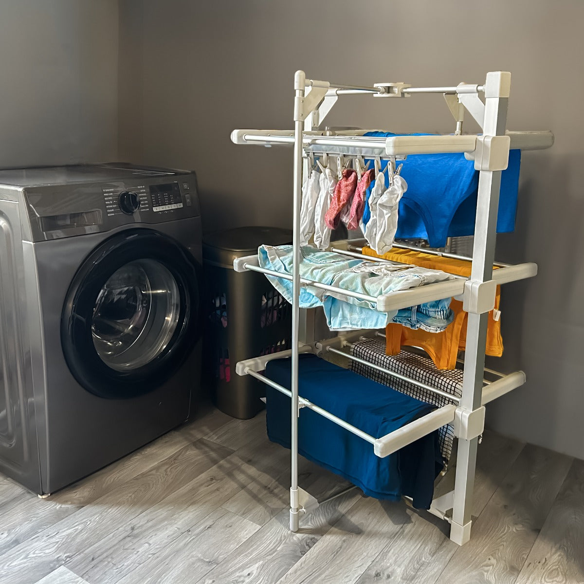 Etendoir à linge électrique chauffant en plastique blanc, avec plusieurs étagères, vêtements colorés suspendus, dans une buanderie moderne