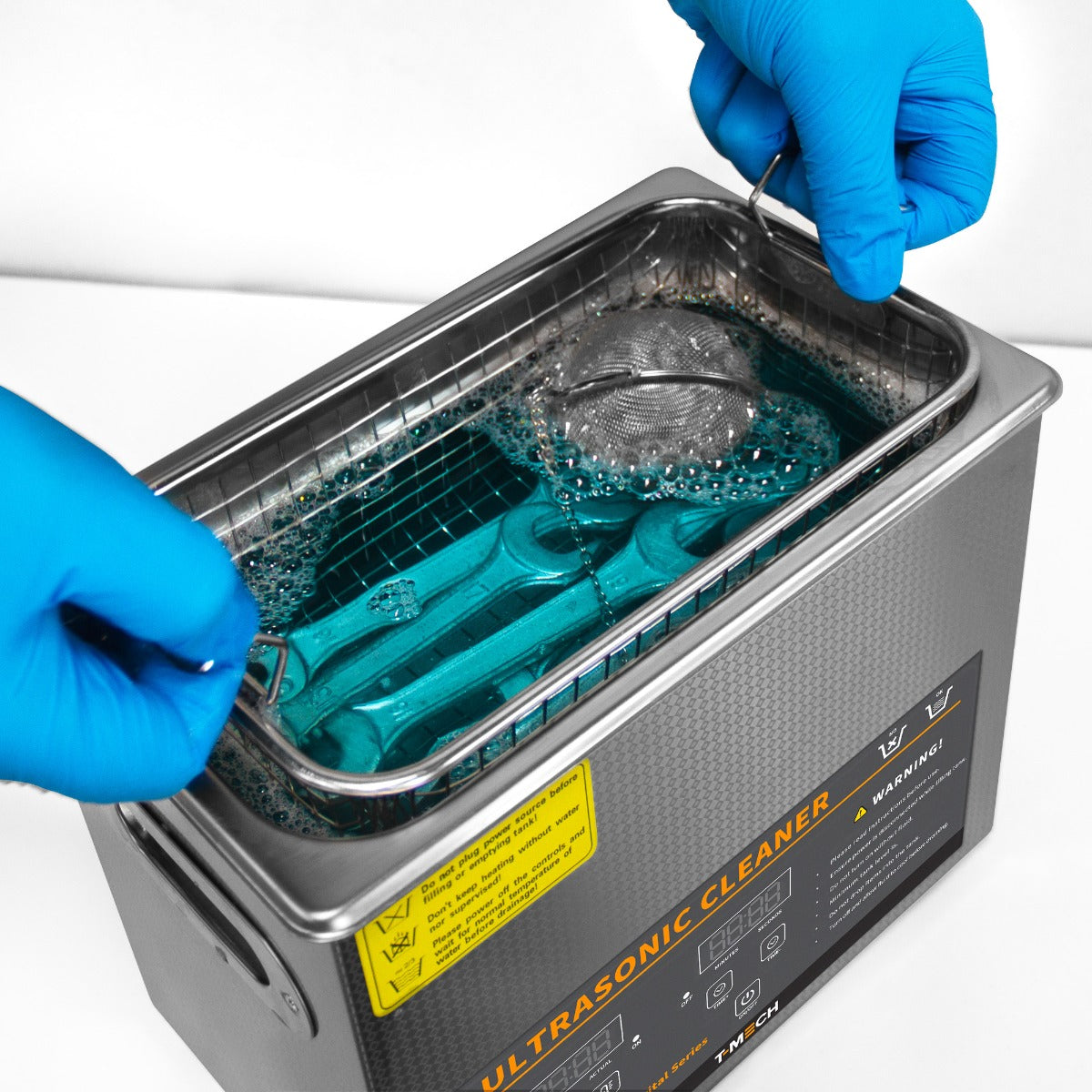 Nettoyeur ultrasonique T-Mech de 6 L avec mains en gants bleus, plongeant des outils dans un liquide bleu pétillant et mousseux