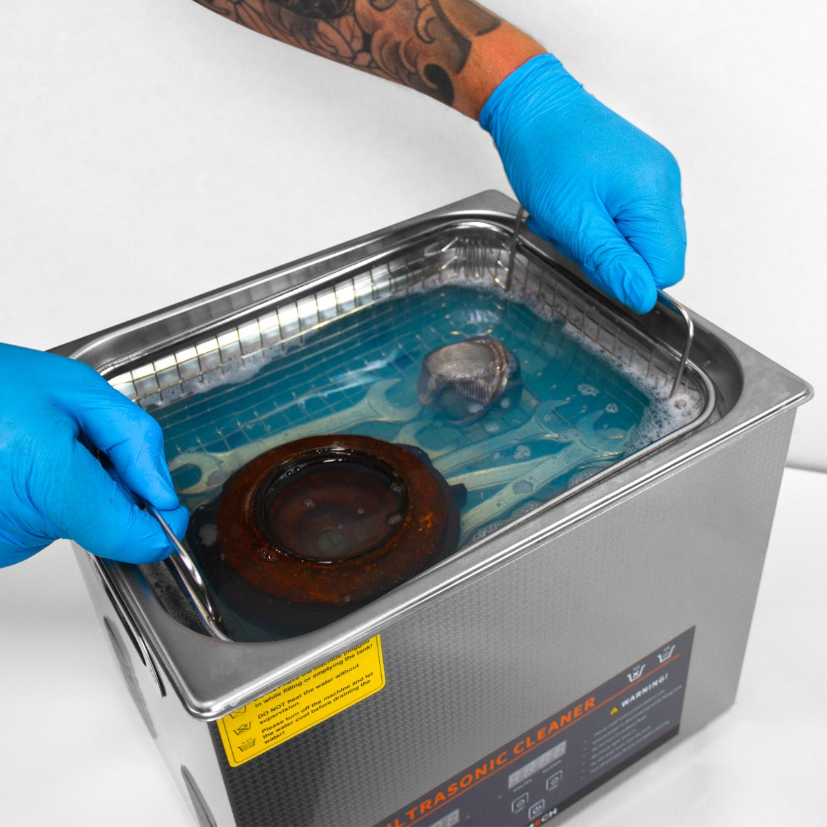 Nettoyeur ultrasonique T-Mech de 10 L avec un récipient en acier inoxydable, eau bleue et pièces métalliques immergées, mains gantées manipulant l'appareil