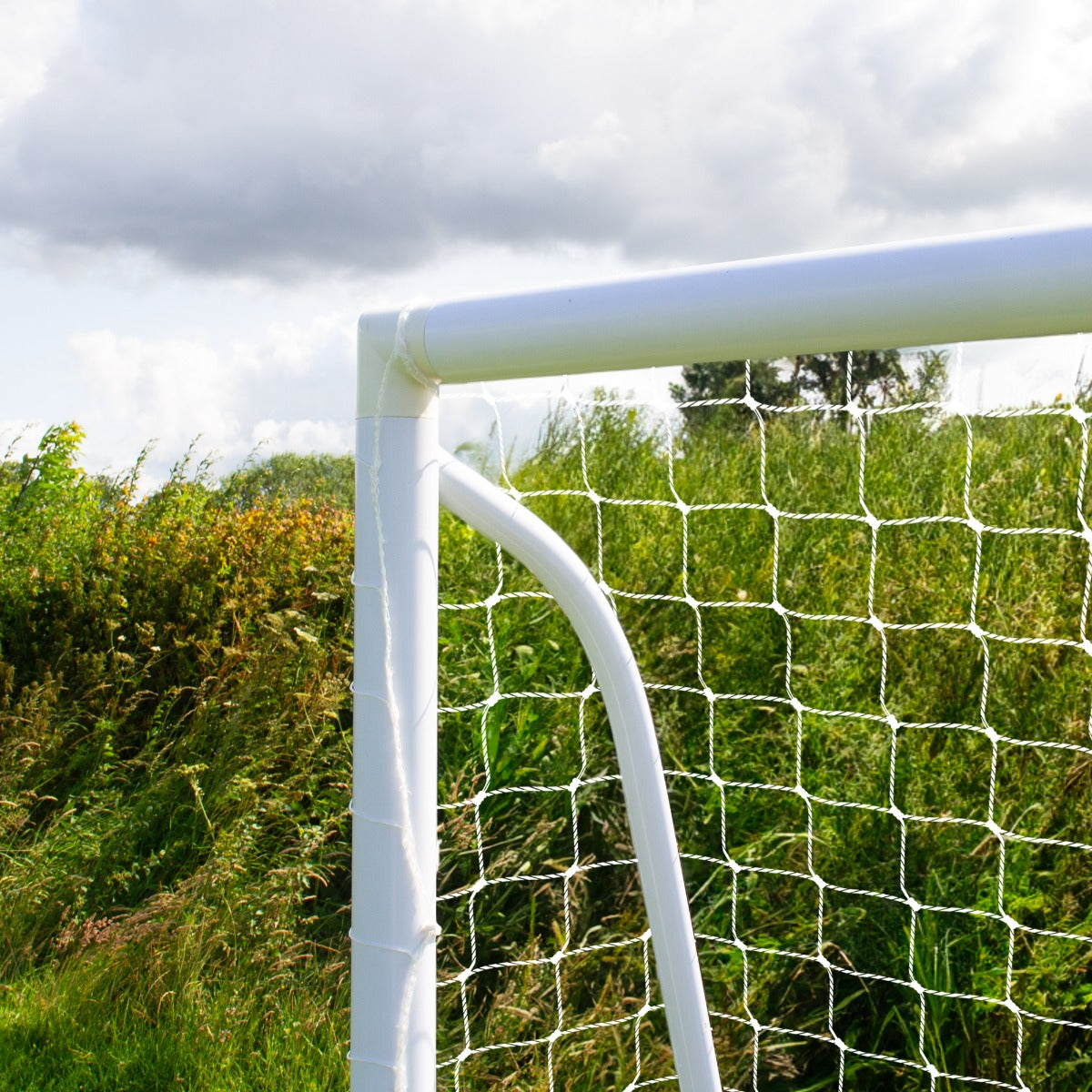But de football 1,8 x 1,2 m avec cadre blanc en plastique, filet en mailles blanches, installé sur un terrain verdoyant sous un ciel nuageux
