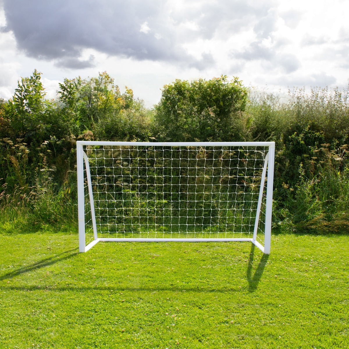 But de football blanc en métal, 1,8 x 1,2 m, avec filet en nylon, installé sur un terrain herbeux sous un ciel nuageux