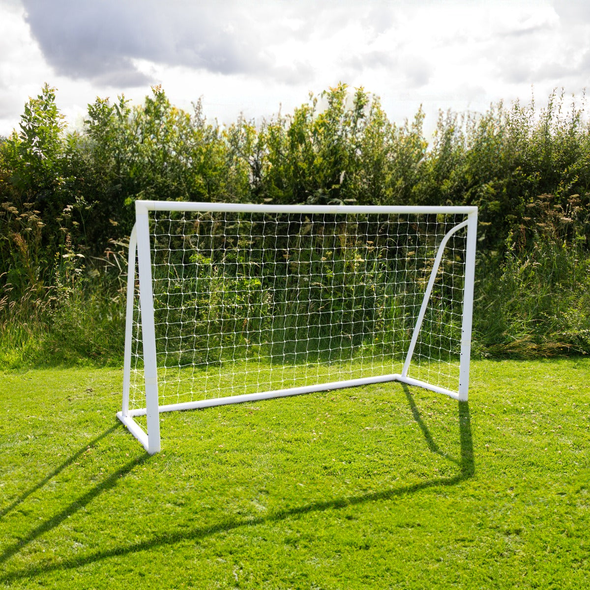 But de football blanc en métal, mesurant 1,8 x 1,2 m, avec un filet transparent, installé sur une pelouse verte sous un ciel nuageux