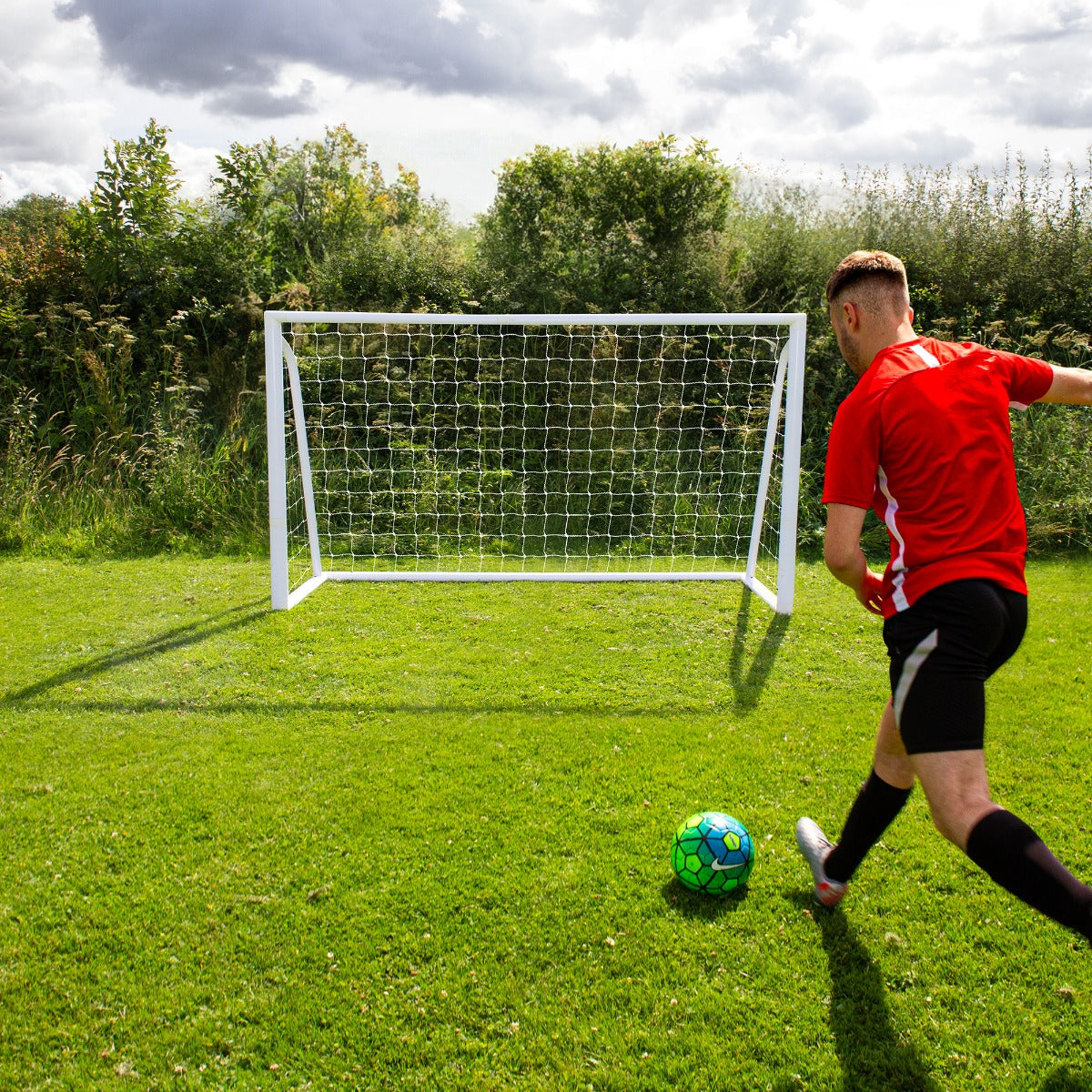 But de football blanc de 1,8 x 1,2 m sur un terrain vert, avec un joueur en maillot rouge tirant un ballon bleu et vert