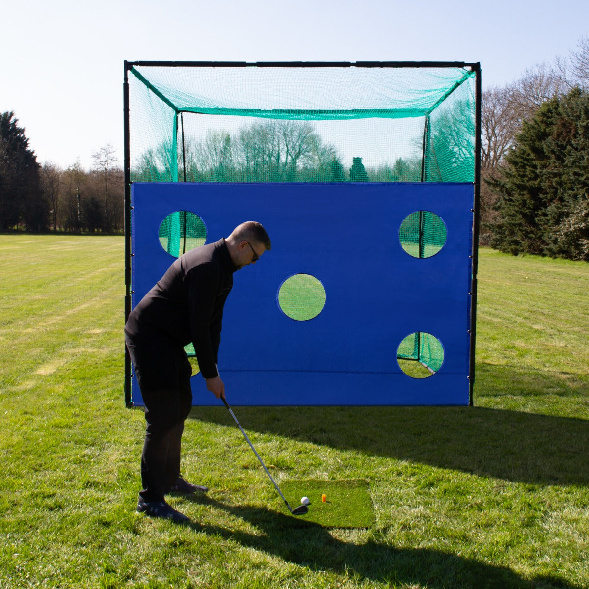 Cage d'entraînement de golf avec une cible bleu vif et plusieurs trous, utilisée sur un terrain gazonné par un golfeur en action