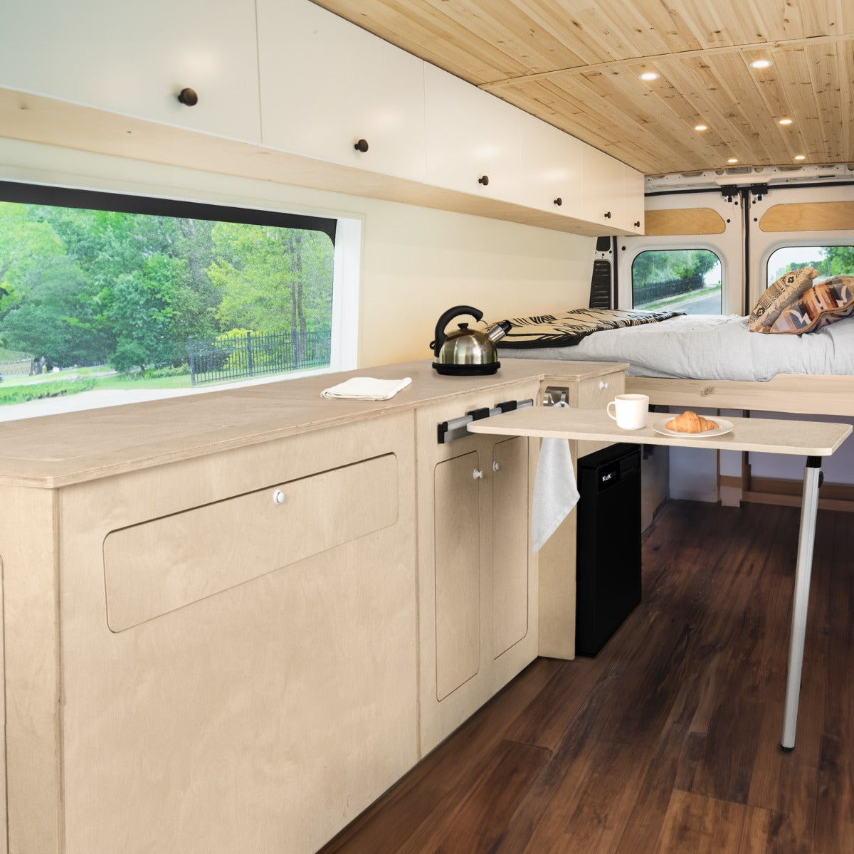 Meuble de cuisine en contreplaqué clair, avec surface lisse, évier intégré et table pliante, dans un camping-car lumineux et spacieux