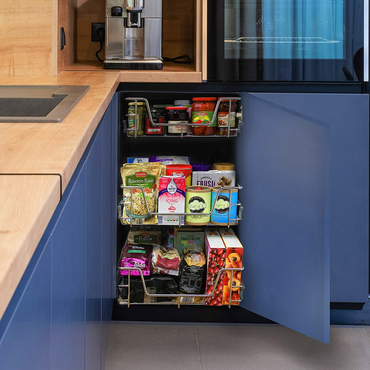 Paniers coulissants en métal argenté, organisant des aliments variés dans un placard de cuisine moderne avec des façades bleues
