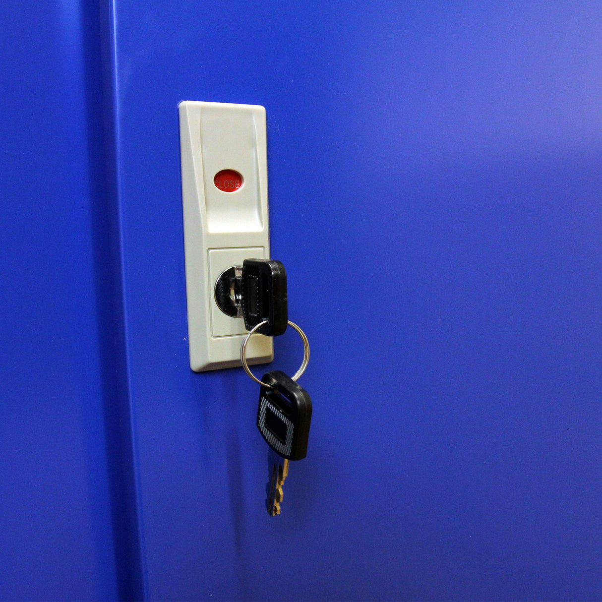 Clé accrochée à un porte-clés noir sur un présentoir de cigarettes bleu, avec un bouton rouge indiquant "fermé