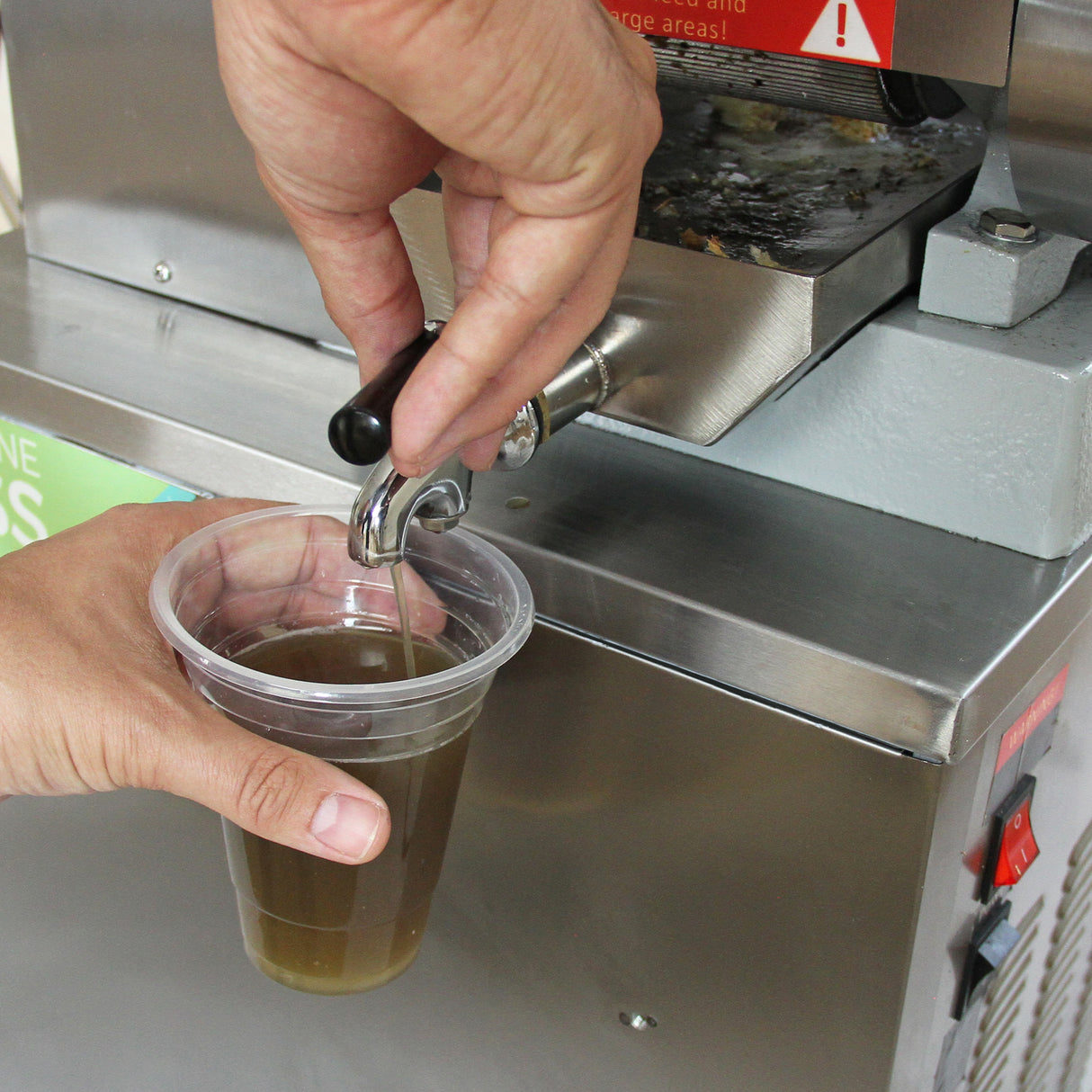Presse à canne à sucre en acier inoxydable, avec un robinet en métal, versant du jus de canne dans un gobelet transparent en plastique