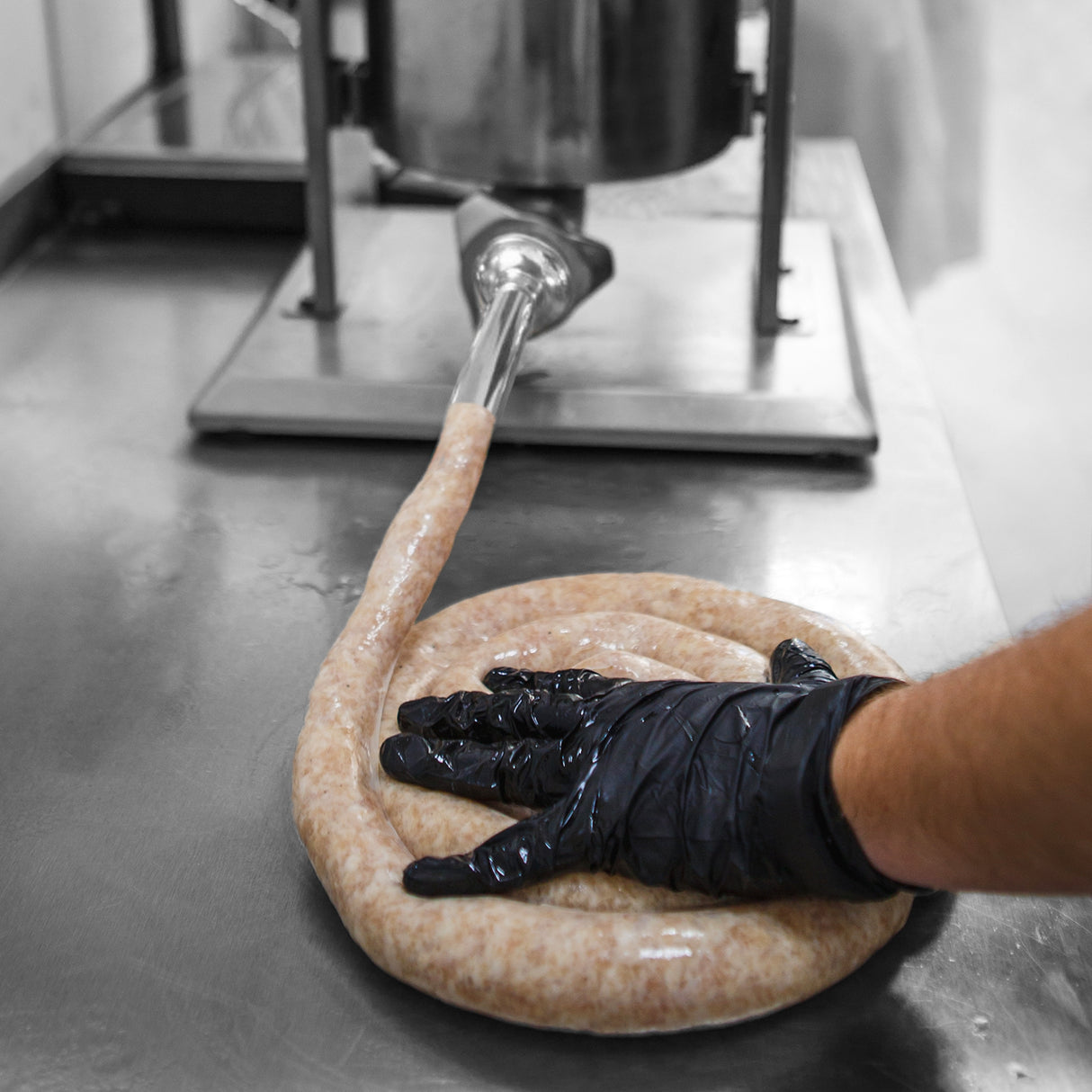 Poussoir à saucisses manuel en acier inoxydable, main gantée pressant une saucisse crue sur une surface de travail en métal