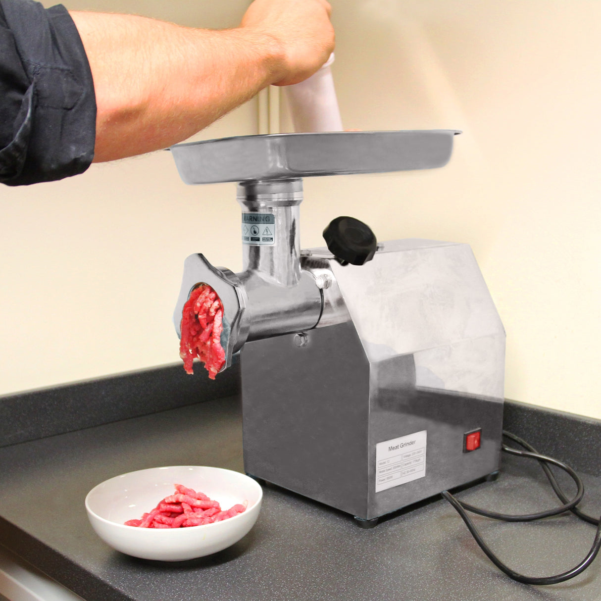 Hachoir à viande commercial en acier inoxydable, avec un moteur puissant, broyant de la viande fraîche dans un bol blanc en céramique