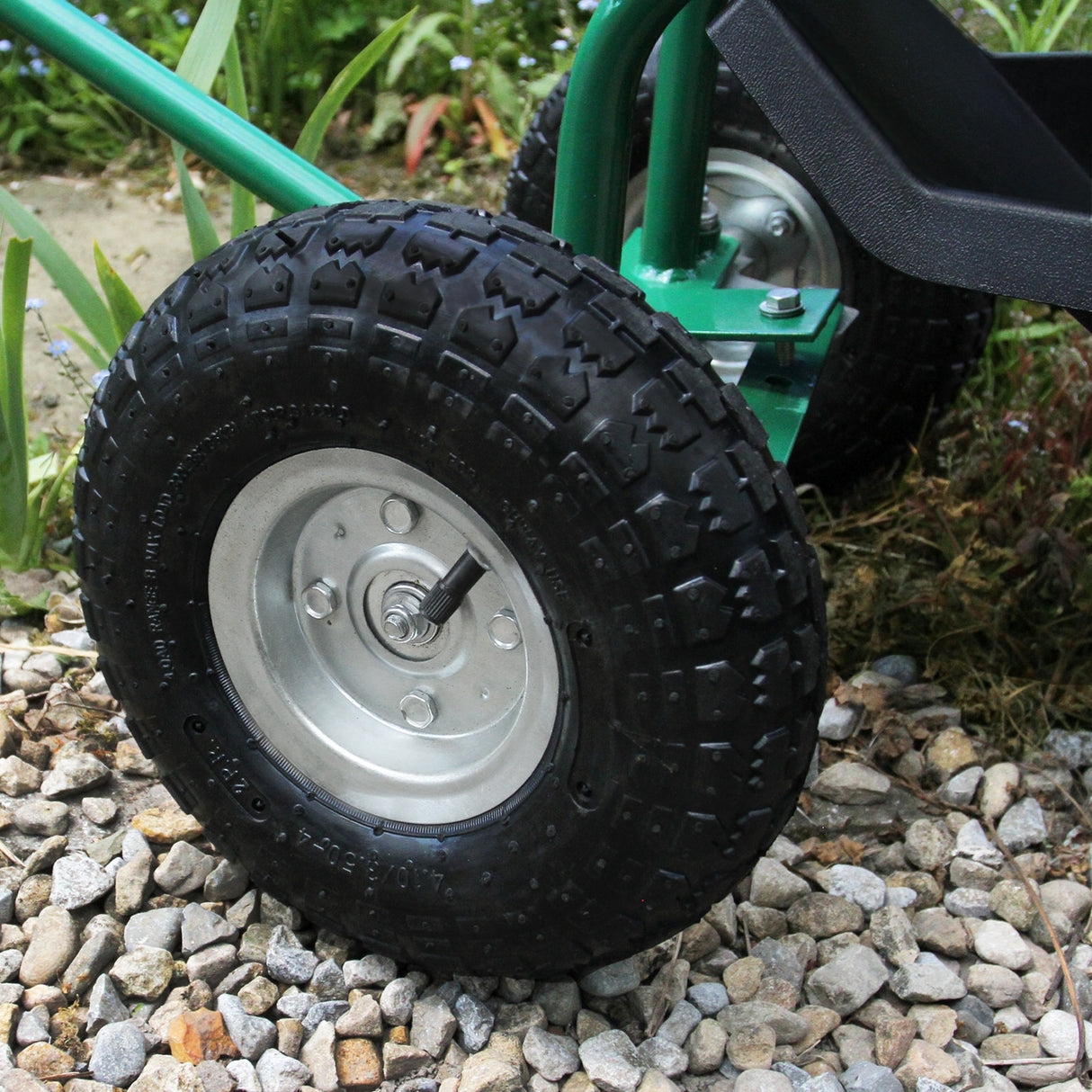 Roue robuste en caoutchouc noir avec jante en métal argenté, conçue pour un siège roulant de jardin, sur un sol en gravier
