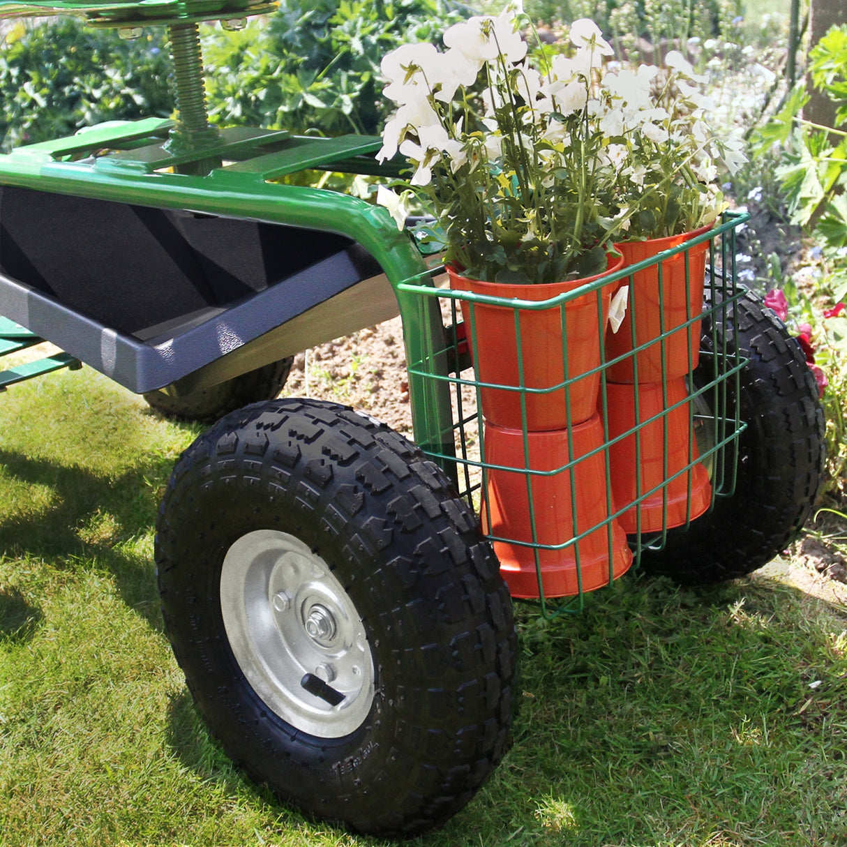 Siège roulant de jardin vert avec panier en métal contenant des pots de fleurs blanches, pneus robustes sur terrain herbeux
