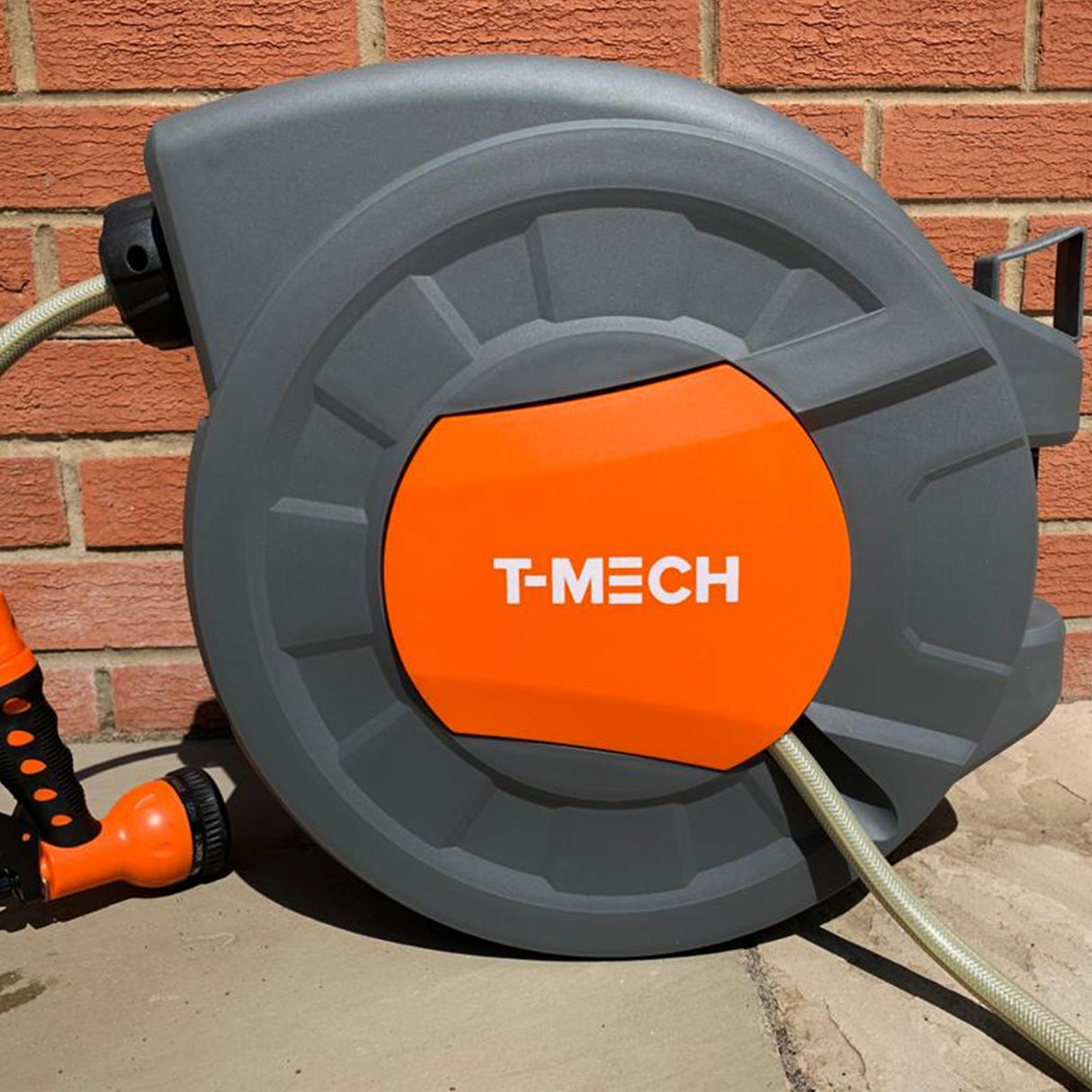 Enrouleur de tuyau d'arrosage de 30 m en plastique gris avec un bouton orange, accompagné d'un pistolet d'arrosage noir et orange