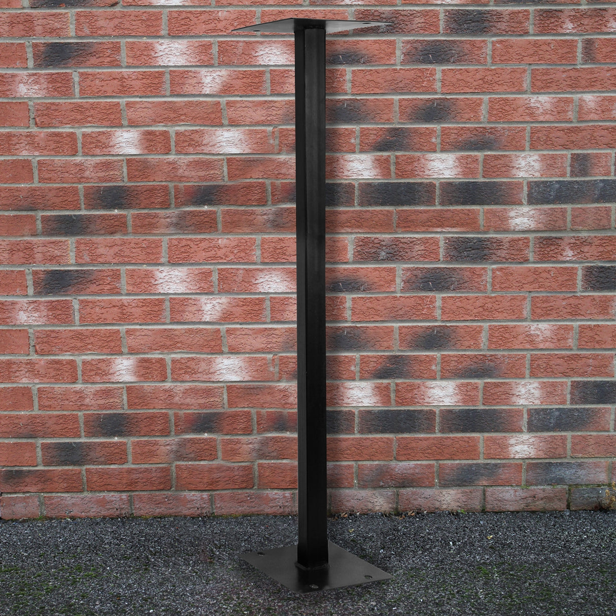 Piédestal en métal noir, élégant et robuste, idéal pour soutenir une boîte aux lettres, posé sur un sol en gravier près d'un mur en briques rouges