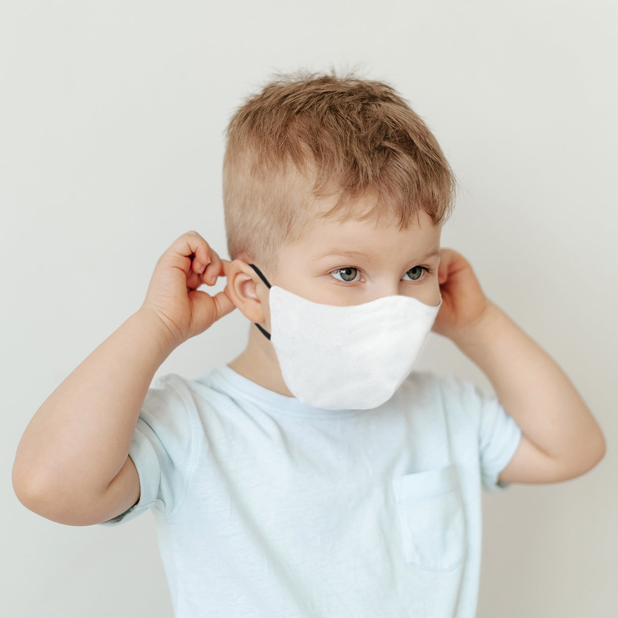 Masque de visage vierge blanc porté par un enfant, avec des oreilles noires, sur un fond neutre, idéal pour la sublimation
