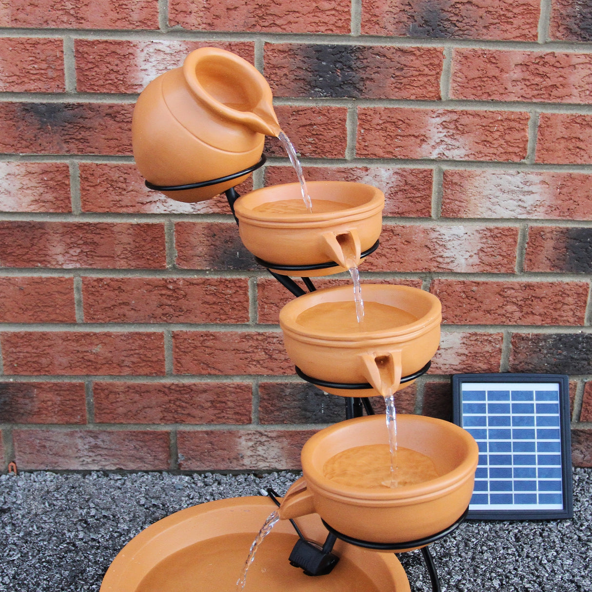 Fontaine de jardin à quatre niveaux en terracotta, avec des pots en terre cuite déversant de l'eau, panneau solaire à côté