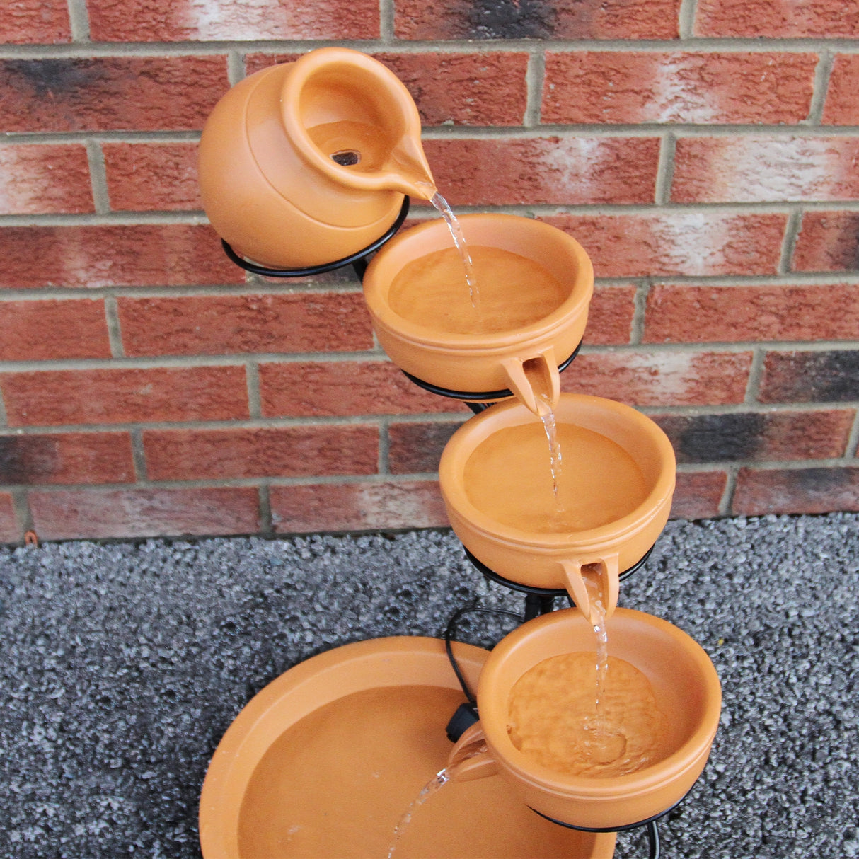 Fontaine de jardin en terracotta à quatre niveaux, avec de l'eau s'écoulant des pots, sur un fond de briques rouges et grises