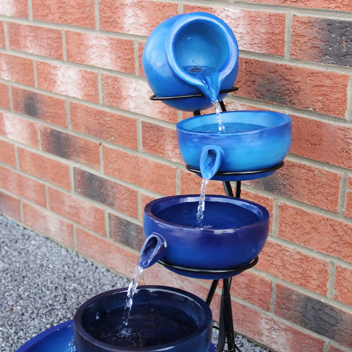 Fontaine de jardin à quatre niveaux en céramique bleue, avec de l'eau s'écoulant des pots vers le bas, sur fond de briques rouges