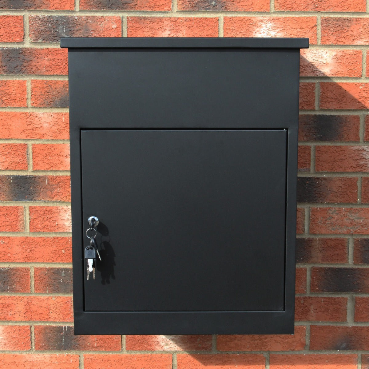 Boîte à colis en métal noir avec une finition lisse, serrure et clé, fixée sur un mur en briques rouges, design moderne et pratique